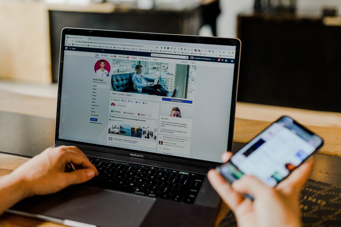 A computer open, showing Facebook, a person holds a phone in their hand too. 